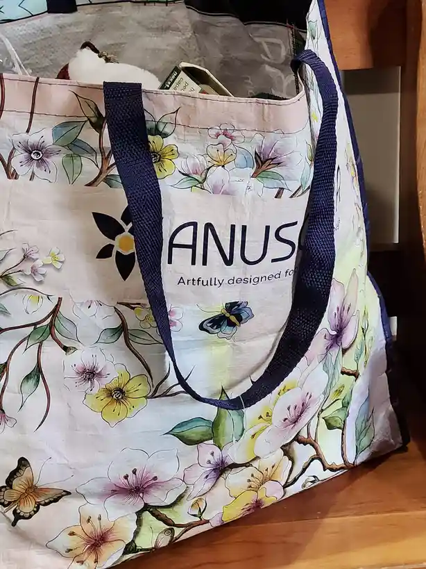 A floral-patterned tote bag with blue straps sits on a wooden surface, partially filled with items. The bag features…
