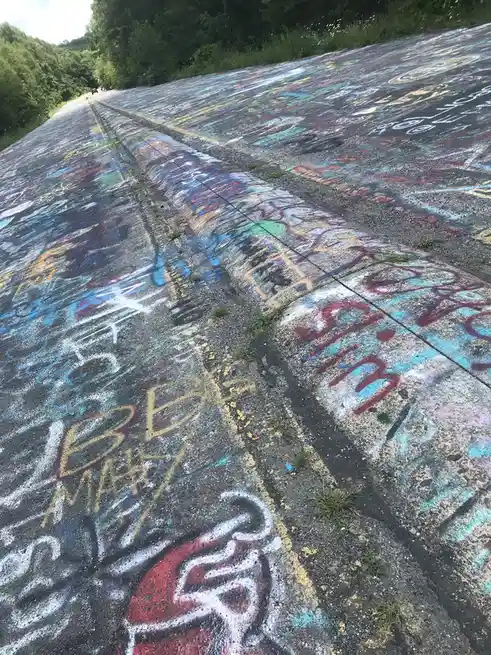 A low-angle shot of a long, sloped concrete surface covered in colorful chalk graffiti, with yellow lines running down the…