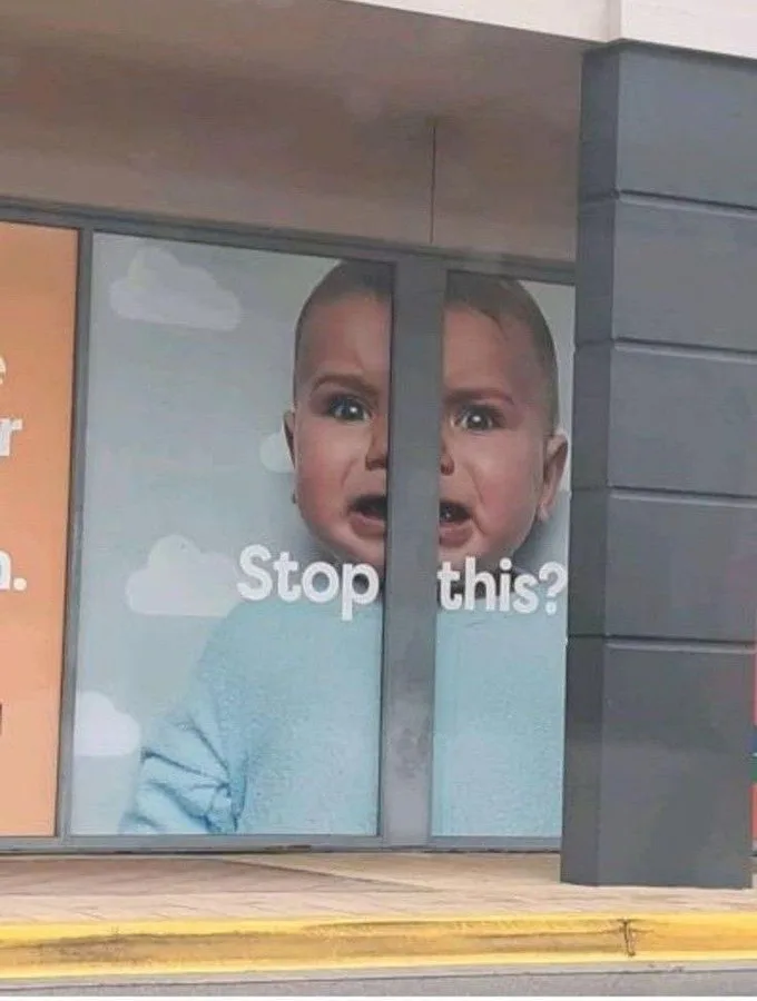 A baby's face is split across two adjacent glass panels of a storefront window, with the baby looking distressed and crying…