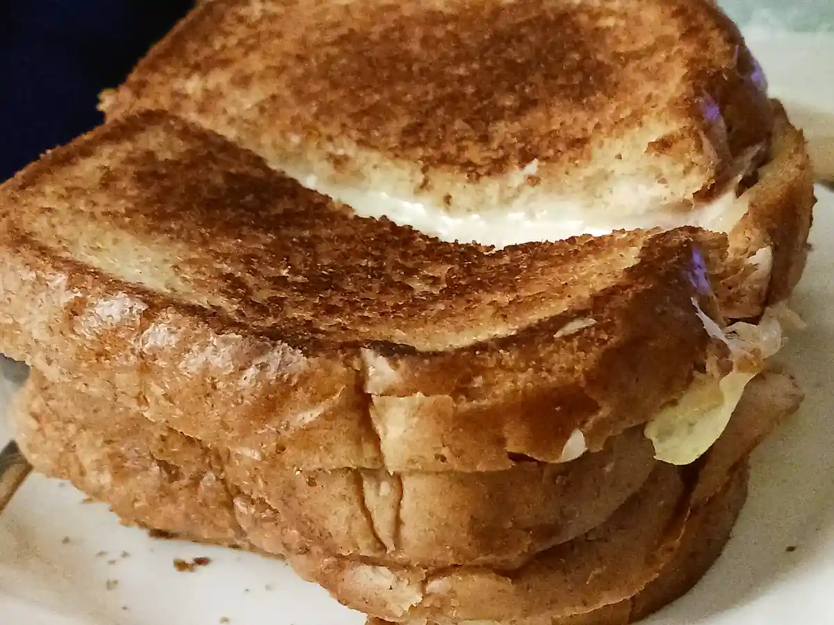 A close-up photo of a golden-brown grilled cheese sandwich with melted cheese oozing slightly from the sides, resting on a…