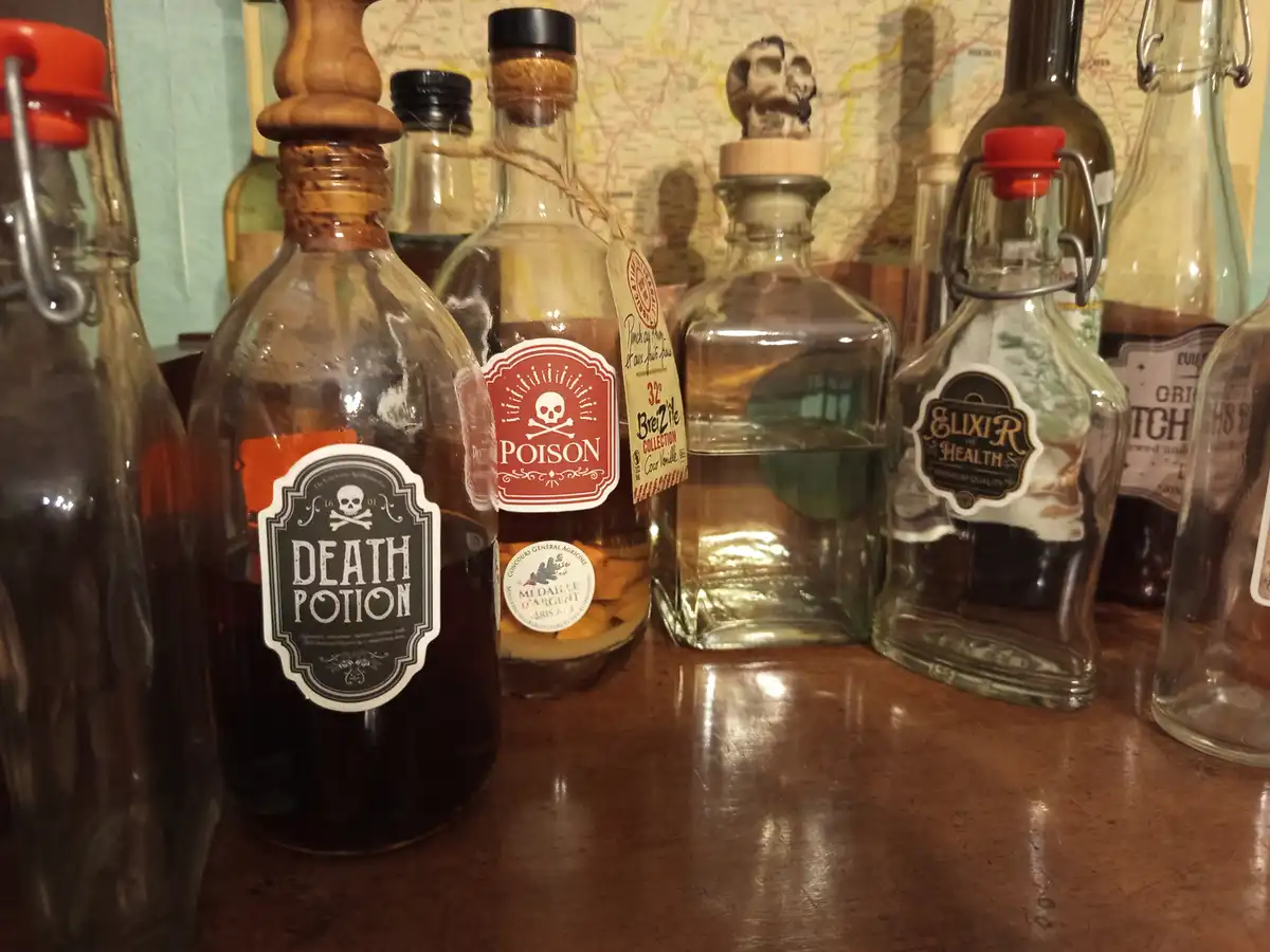 A row of glass bottles on a wooden surface, some labeled with skull-and-crossbones or ominous names like 'Death Potion' and…