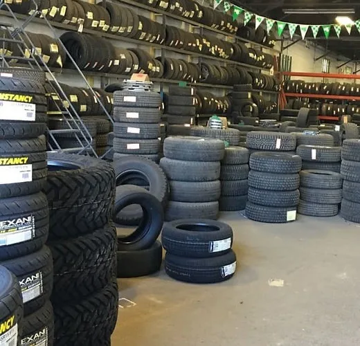 A warehouse filled with stacks of black tires on shelves and the floor, with green and white pennant banners hanging from…