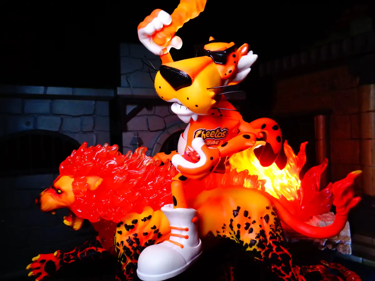 A stylized figurine of the cartoon character Cheetos, depicted as a fiery orange cheetah wearing sunglasses and a…