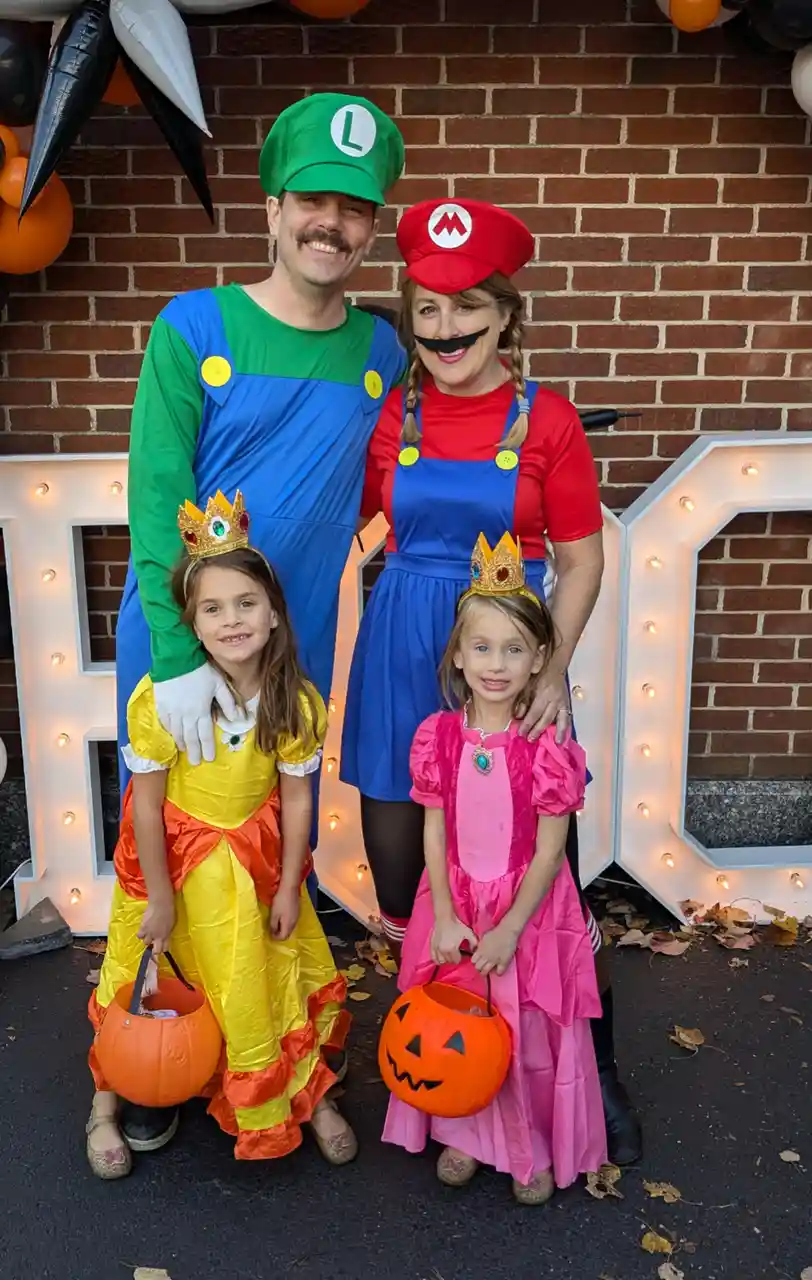 A family of four dressed in Mario and Luigi Halloween costumes poses for a photo. The father wears a green Luigi outfit, the…