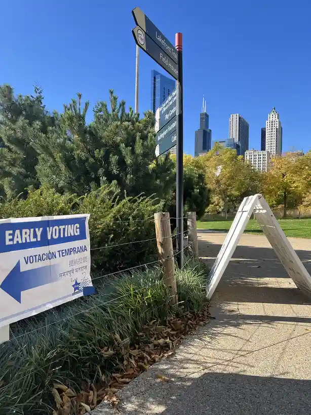 A photo shows a blue and white 'EARLY VOTING' sign in English, Spanish, Chinese, and Hindi, pointing left, placed beside a…