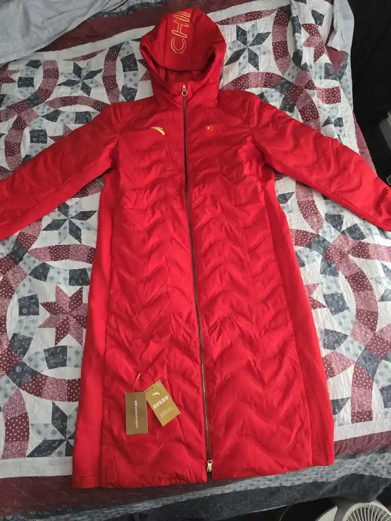 a bright red, full-length hooded winter jacket with a gold zipper, Chinese flag patch, and 'CHN' on the hood lies flat on a…