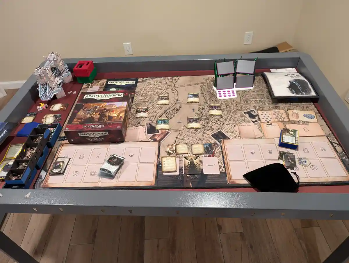 An overhead shot of a large, grey gaming table set up for playing 'Arkham Horror: The Card Game,' featuring the 'The Scarlet…
