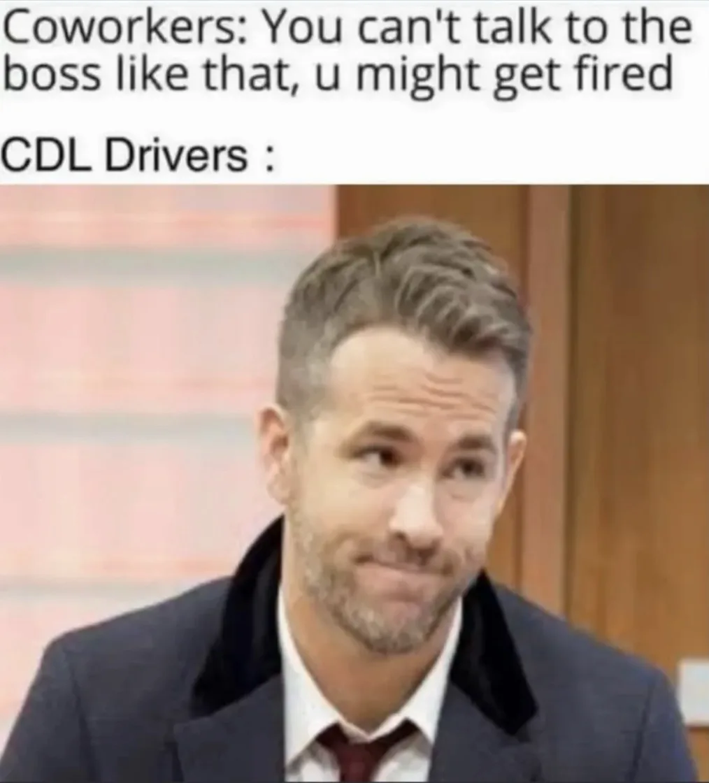 The image shows actor Ryan Reynolds looking sideways with a smug, unimpressed expression while wearing a suit and tie. The…