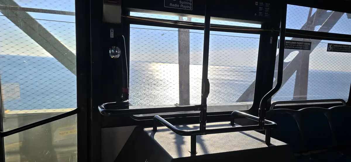 The image shows the interior of a public transit vehicle, likely a ferry or bus, with empty seats and handrails. Through the…
