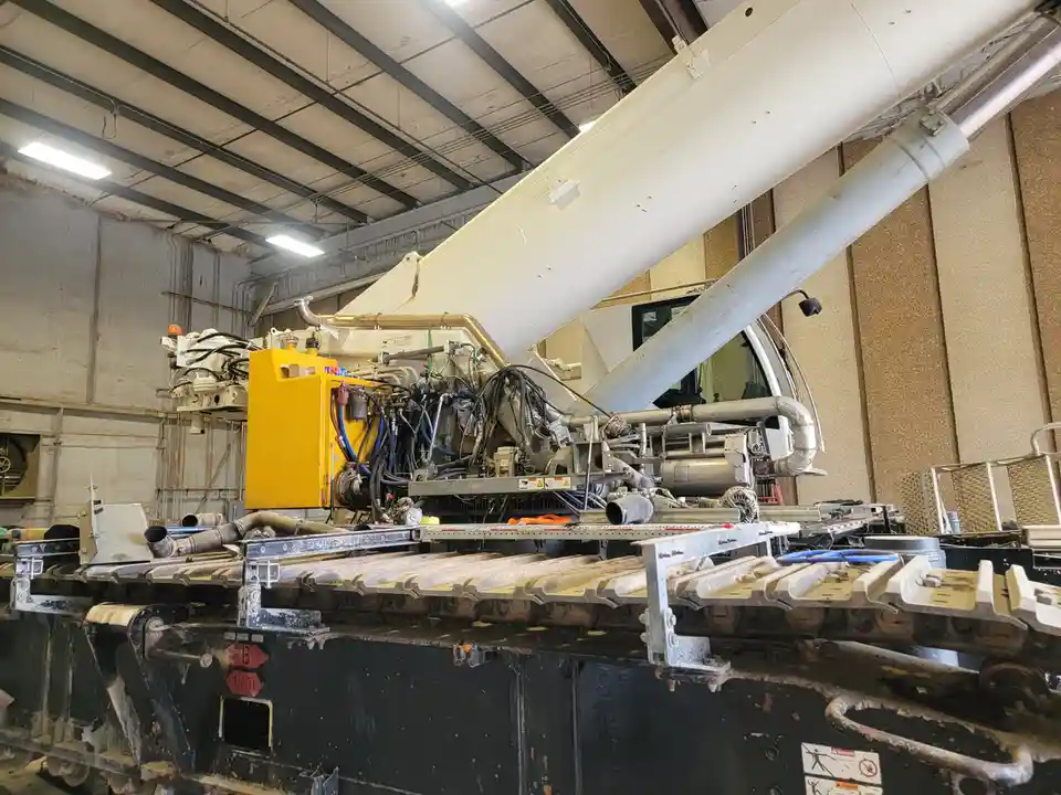 A large, complex piece of industrial machinery, possibly a crane or excavator, is shown inside a warehouse with exposed…