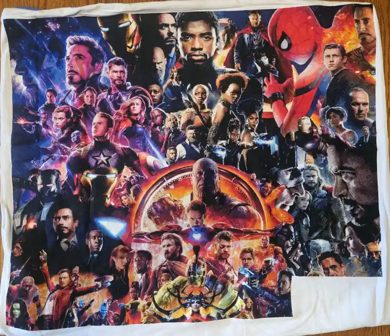 A white towel is laid flat on a wooden surface, printed with a dense collage of Marvel superhero characters from the…