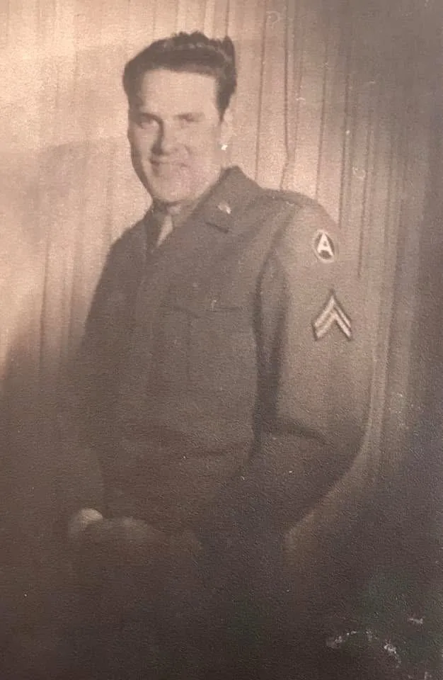 A sepia-toned, grainy vintage photograph shows a man in a military uniform with a sergeant's chevron and an 'A' patch on his…