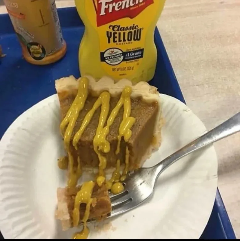 A slice of pie on a paper plate with a fork, drizzled with yellow mustard from a French's Classic Yellow Mustard bottle…