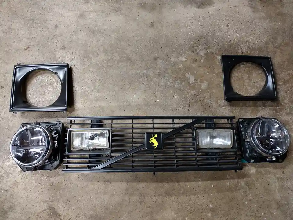 A disassembled Volvo front grille with its headlights and mounting brackets laid out on a concrete floor. The grille…