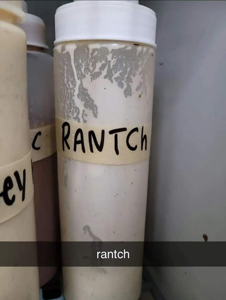A close-up of a white squeeze bottle with a handwritten label that reads 'RANTCH' in black marker, placed among other…
