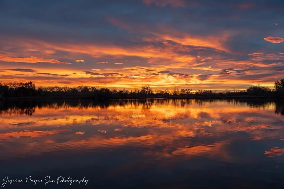 A serene landscape photograph shows a vibrant sunset with orange and purple clouds reflected in a calm body of water…
