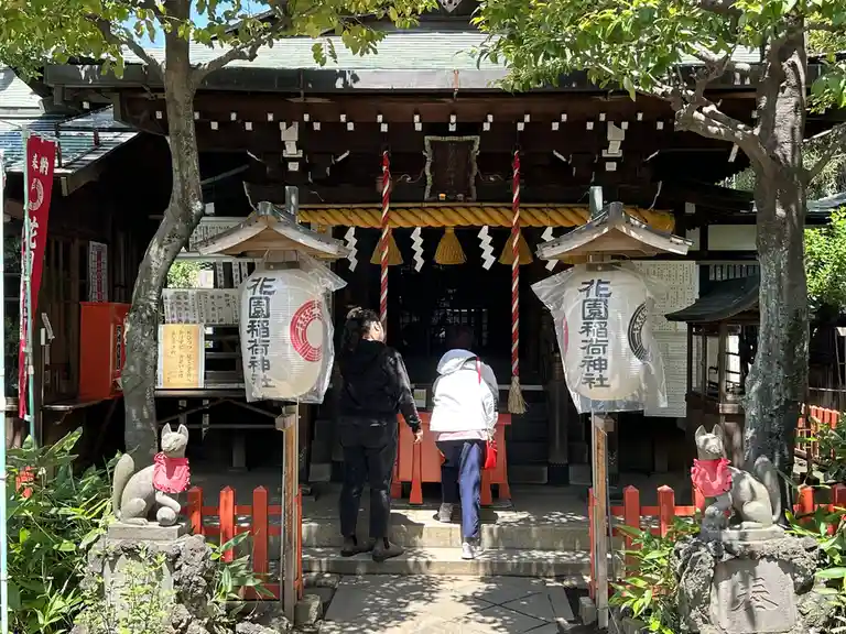 Two people stand at the entrance of a traditional Japanese shrine, facing the inner sanctum under a large rope barrier…