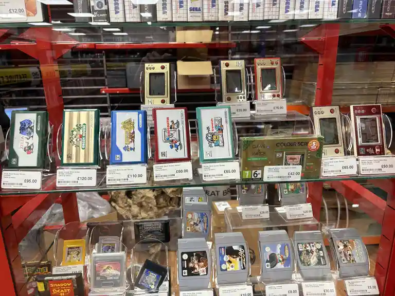 A glass display case in a store shows vintage Nintendo Game & Watch handhelds and Game Boy cartridges with price tags. The…
