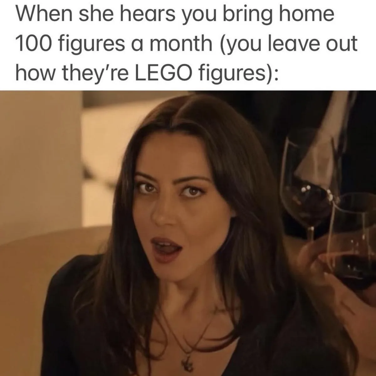 A woman with long dark hair, wearing a black top and a necklace, stares with wide eyes and an open mouth in shock. Behind…