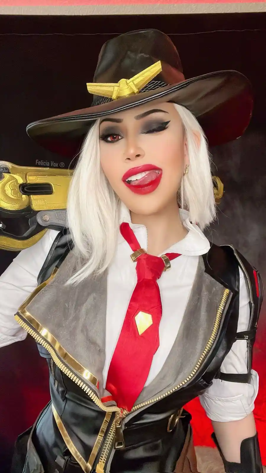A person in a detailed cosplay of the video game character Ashe from Overwatch, wearing a brown hat with a gold emblem…