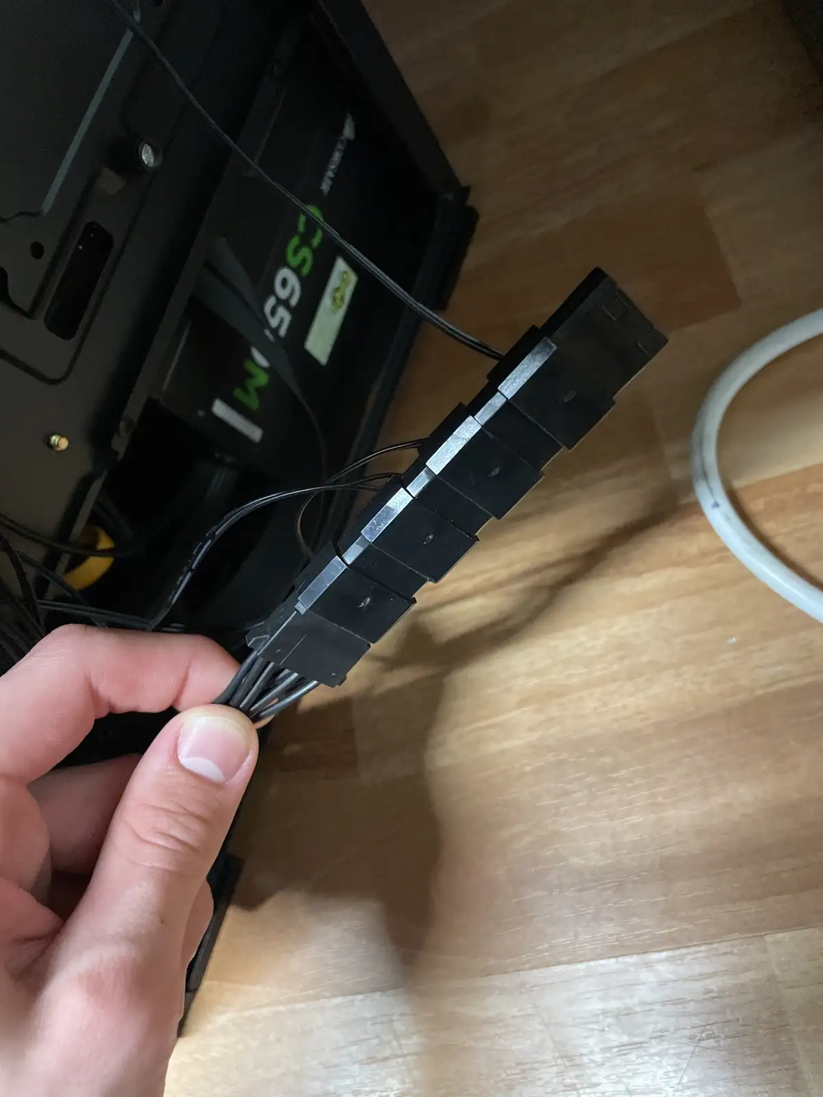 A hand holds a bundle of black computer cables secured with a black plastic cable tie against a wooden floor. Behind the…