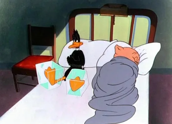 daffy duck sits on a bed next to a sleeping character, holding two transparent cubes with orange duck-shaped objects inside…