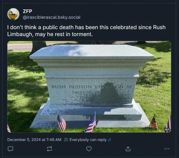 A photo of a tombstone for Rush Hudson Limbaugh III, with American flags placed at its base. The tombstone is made of…