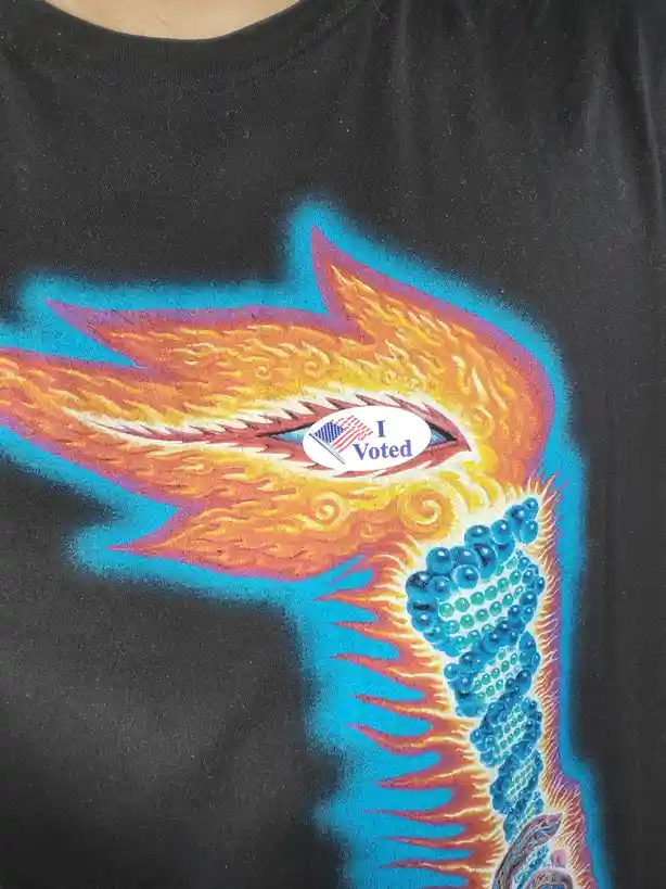 A close-up of a black t-shirt featuring a psychedelic, flame-like phoenix design with vibrant orange, yellow, and blue…