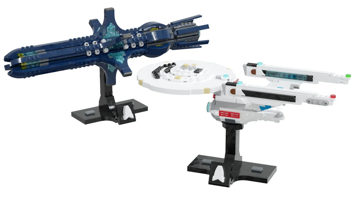 Two LEGO Star Trek starships, a blue Klingon Bird-of-Prey and a white Starfleet ship, are displayed on black stands against…