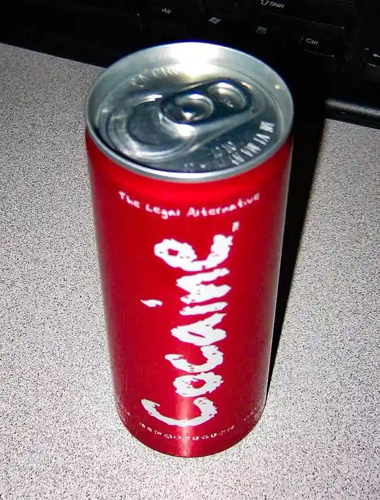 A red soda can with a silver pull-tab lid sits on a speckled gray surface, with a black keyboard partially visible in the…