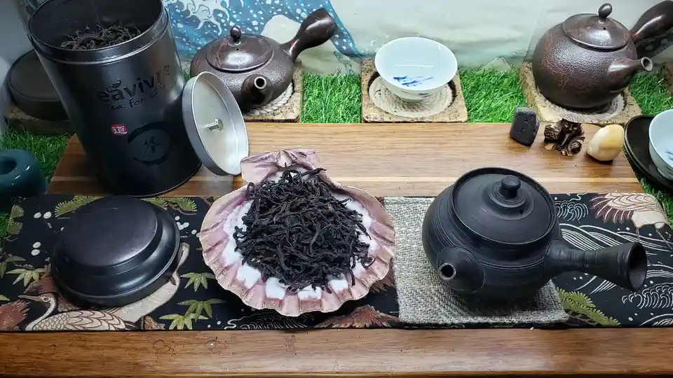 A wooden table displays an elaborate tea setup with multiple dark teapots, a white teacup, and a large black 'Teavivre' tea…
