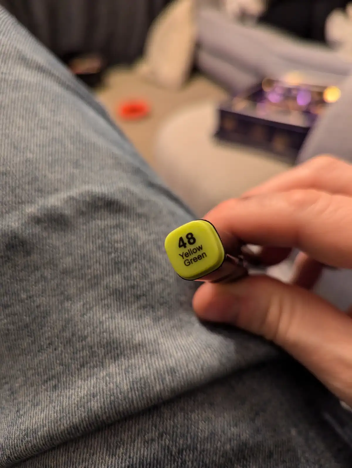 A close-up photo shows a hand holding a yellow-green colored marker, labeled '48 Yellow Green', against a background of grey…