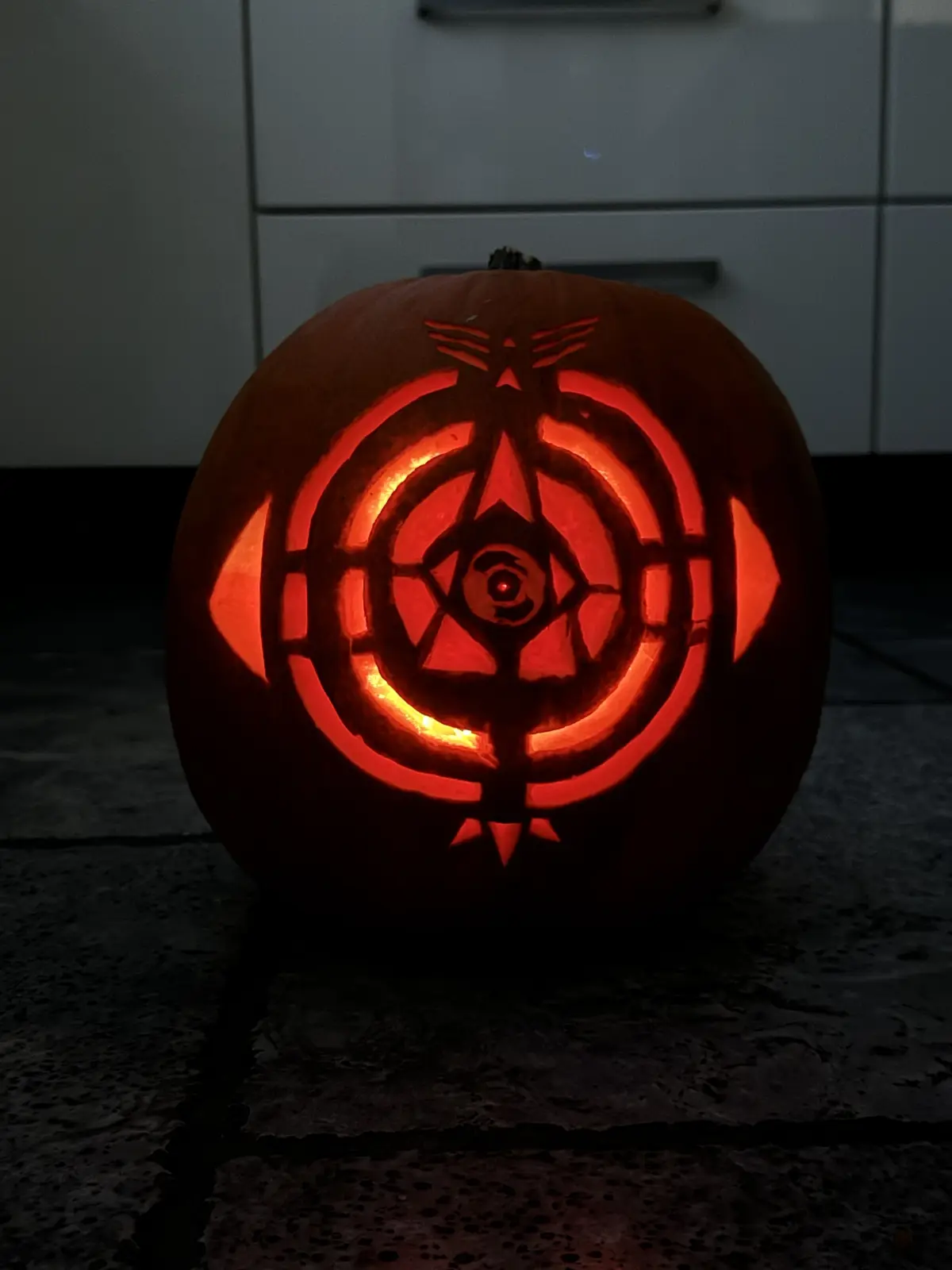 A carved Halloween pumpkin with an intricate glowing design resembling the Eye of the Storm symbol from the game 'The Outer…