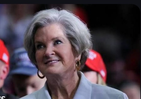 a close-up photo of an older woman with gray hair and a slight smile, looking upward and to her right. She wears a…