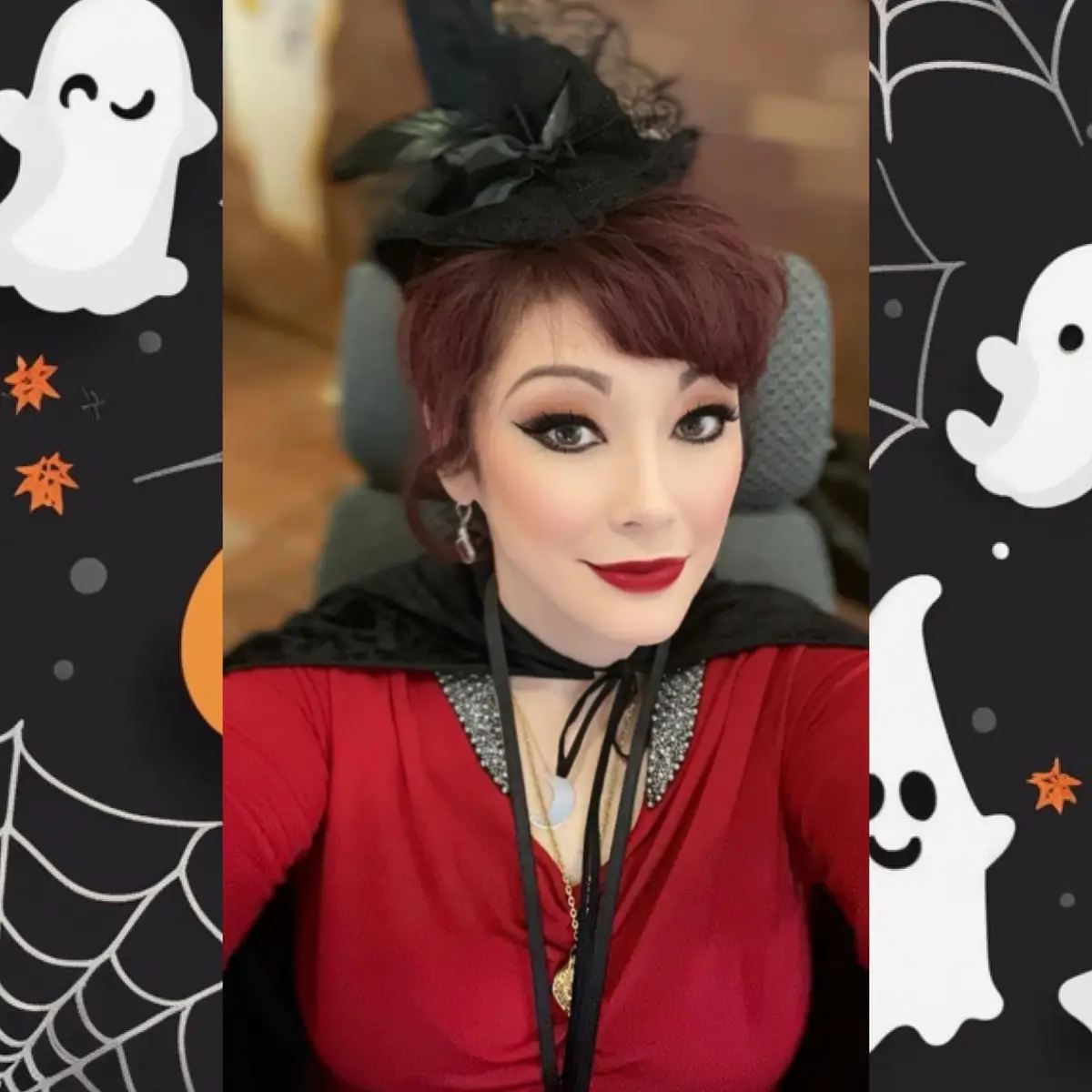 A person with short red hair, heavy makeup, and a black witch hat poses in a red dress with a black cape, surrounded by…