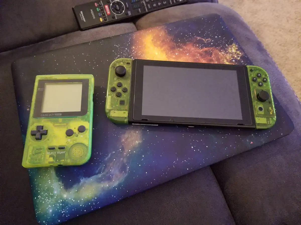 A green translucent Game Boy Pocket and a green translucent Nintendo Switch with its Joy-Cons attached are placed…