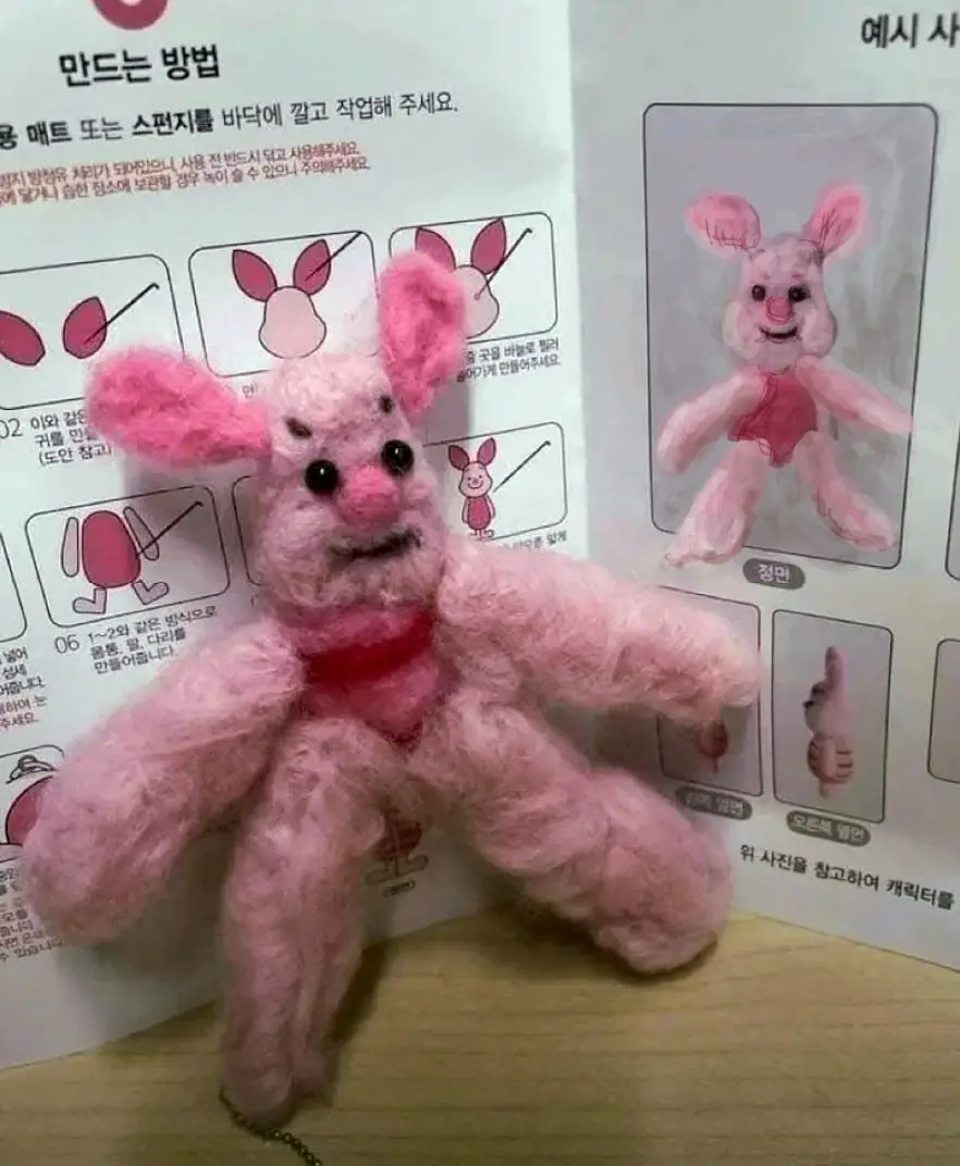 A pink, fuzzy, needle-felted bunny toy with a distorted, angry-looking face sits in front of a Korean-language craft…