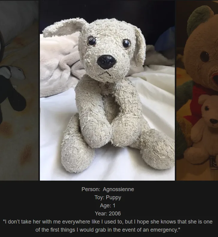 A close-up photo of a well-worn, light gray plush puppy toy sitting upright on a white blanket. The toy has dark button eyes…