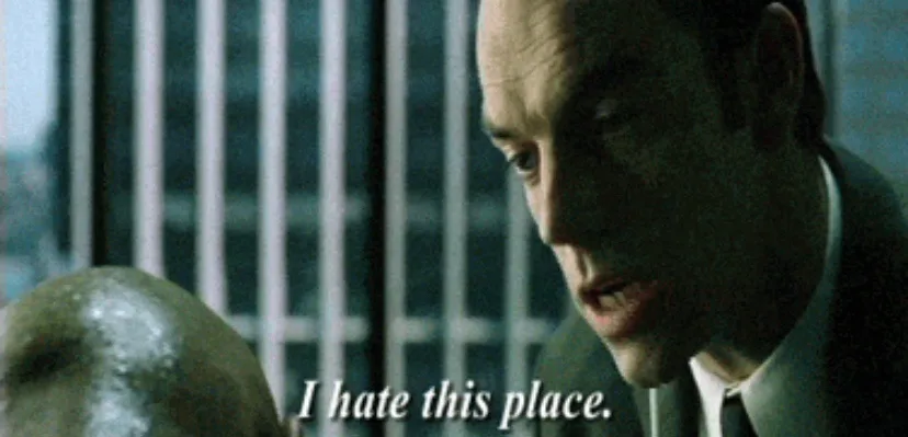 A close-up shot of a man in a suit looking down at another person's bald head, with the text 'I hate this place.' overlaid…