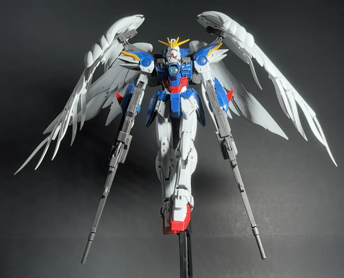 A detailed plastic model of a white, blue, and red mobile suit with large, spread white wings and two long grey weapons…
