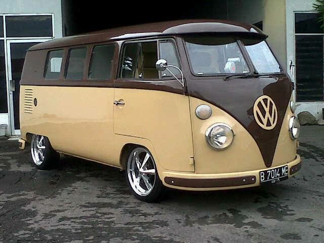 A vintage two-tone Volkswagen Type 2 van, painted beige and brown, is parked outdoors. It has modern chrome wheels and a…