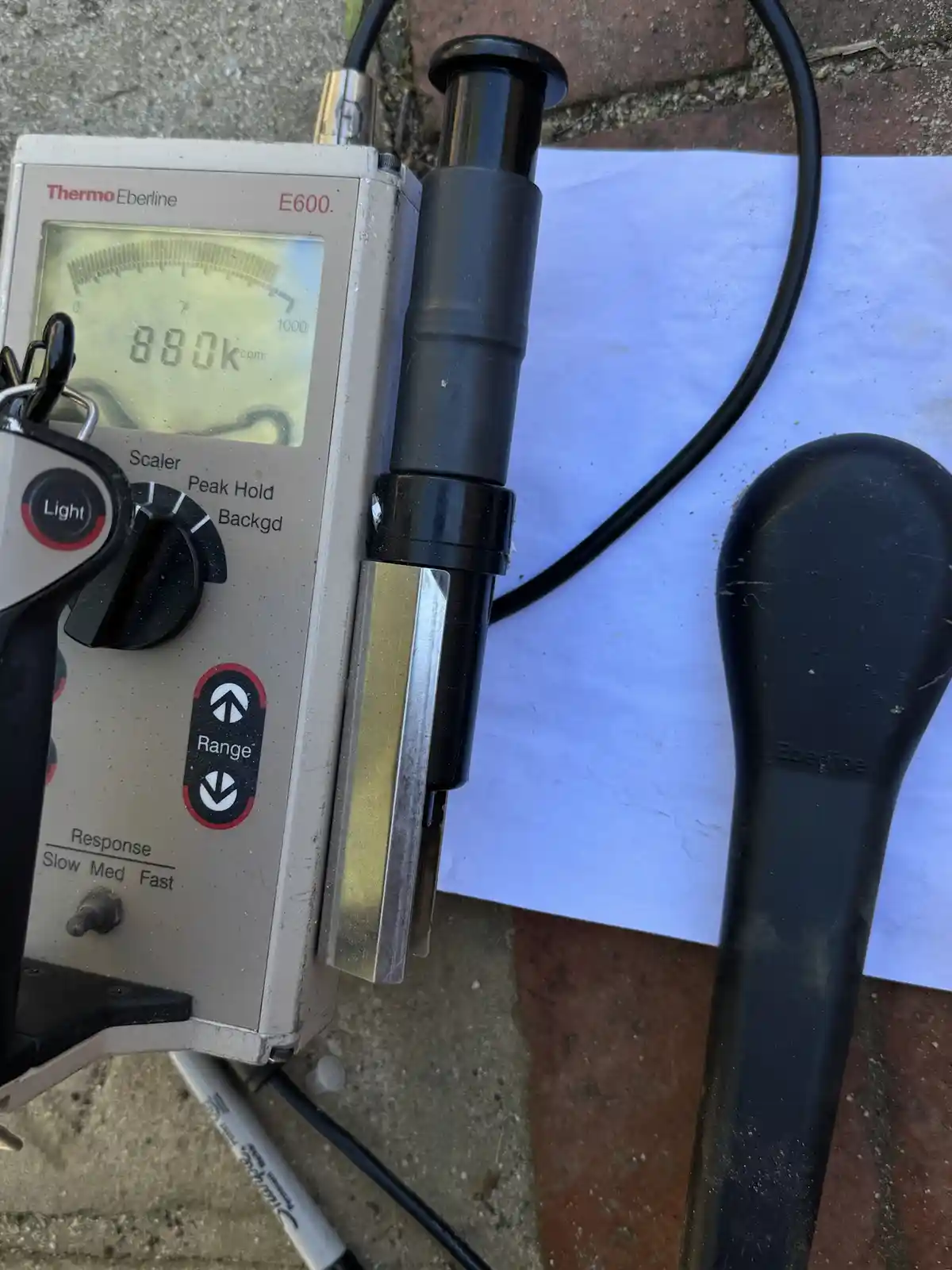 A close-up photo of a Thermo Eberline E600 radiation detector with its digital display showing '880k cpm'. The device has a…