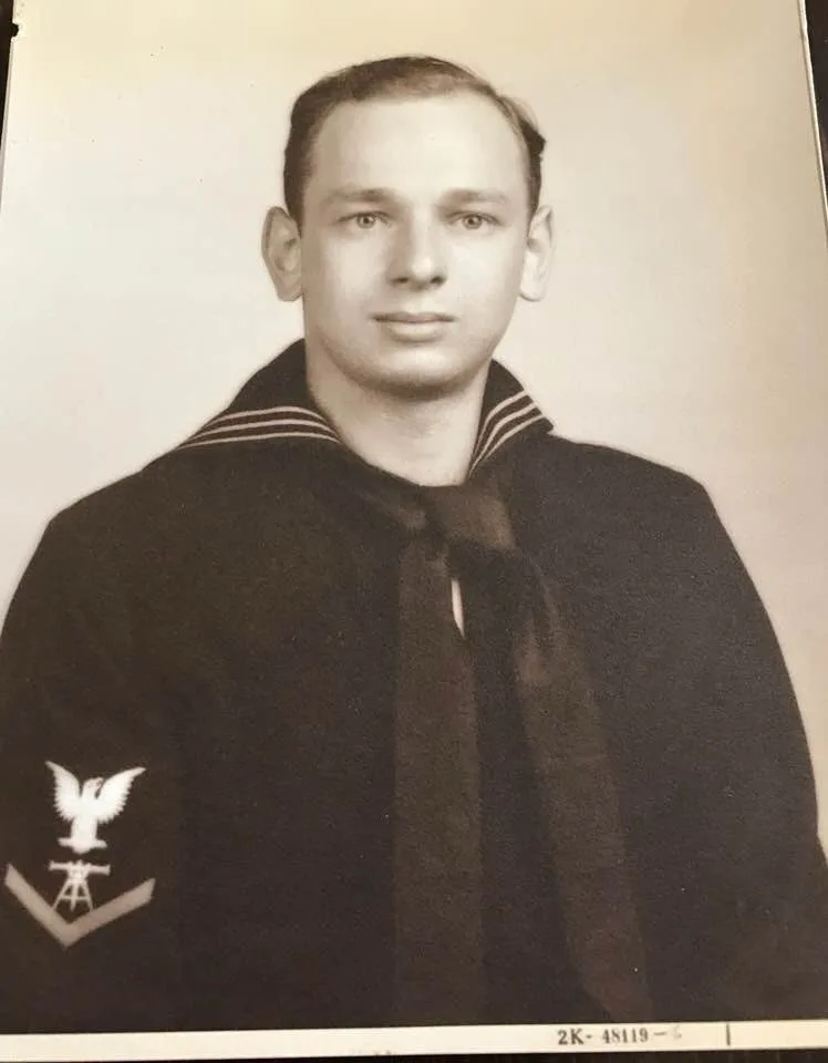 A black-and-white vintage military portrait of a young man in a dark sailor-style uniform with a neckerchief and a rank…