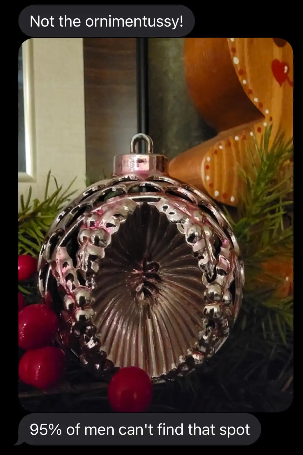 A close-up photo of a silver, ornate Christmas ornament with a decorative pattern, surrounded by green pine needles and red…