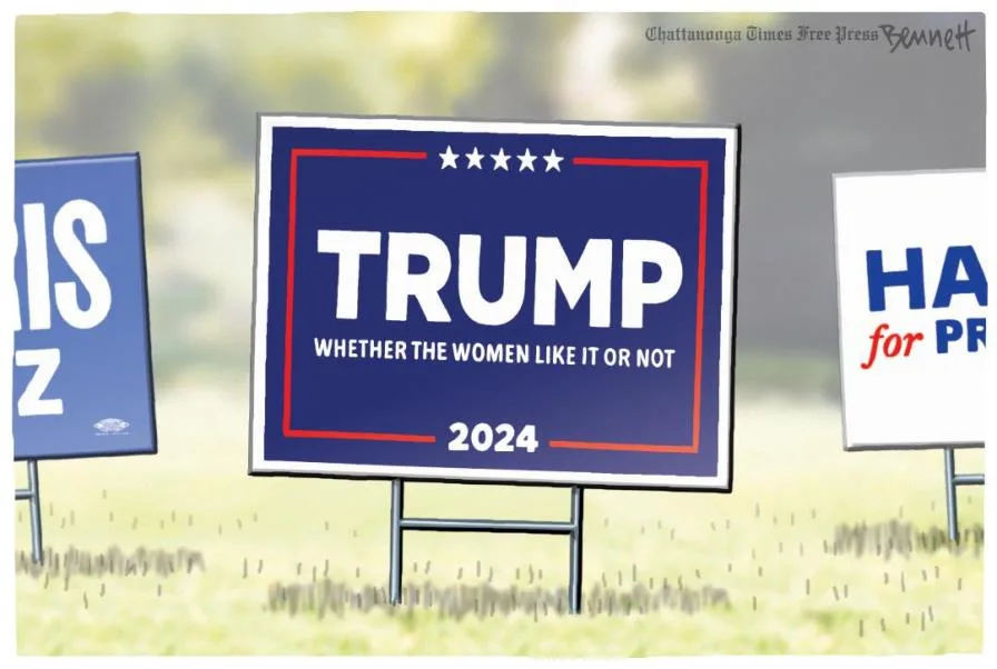 A cartoon image shows three political campaign signs in a grassy field. The central, largest sign is blue with a red border…