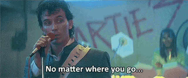 A still image from the movie 'The Commitments' shows a man singing into a microphone with a guitar strap over his shoulder…