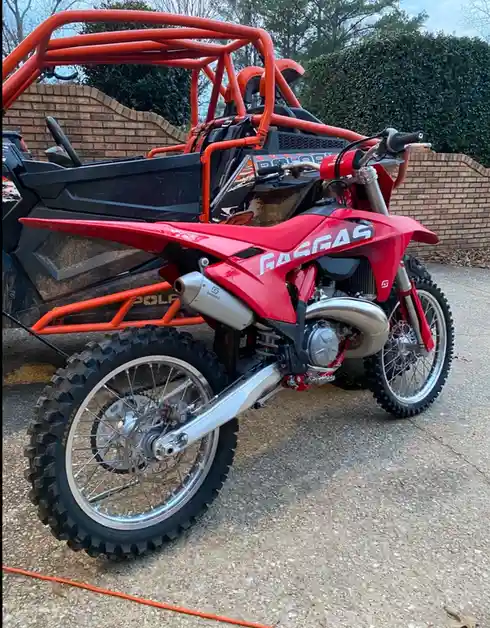 A red GasGas dirt bike is parked in front of an orange Polaris Ranger side-by-side utility vehicle, both on a concrete…