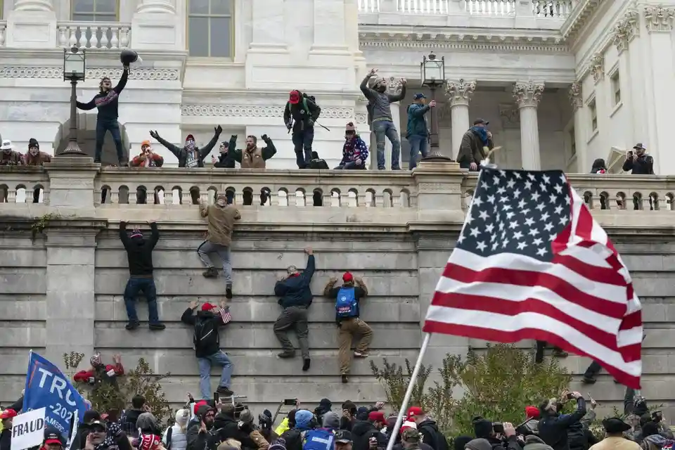 A photo shows protesters scaling the stone steps of the U.S. Capitol building, with some already on the upper balcony. An…