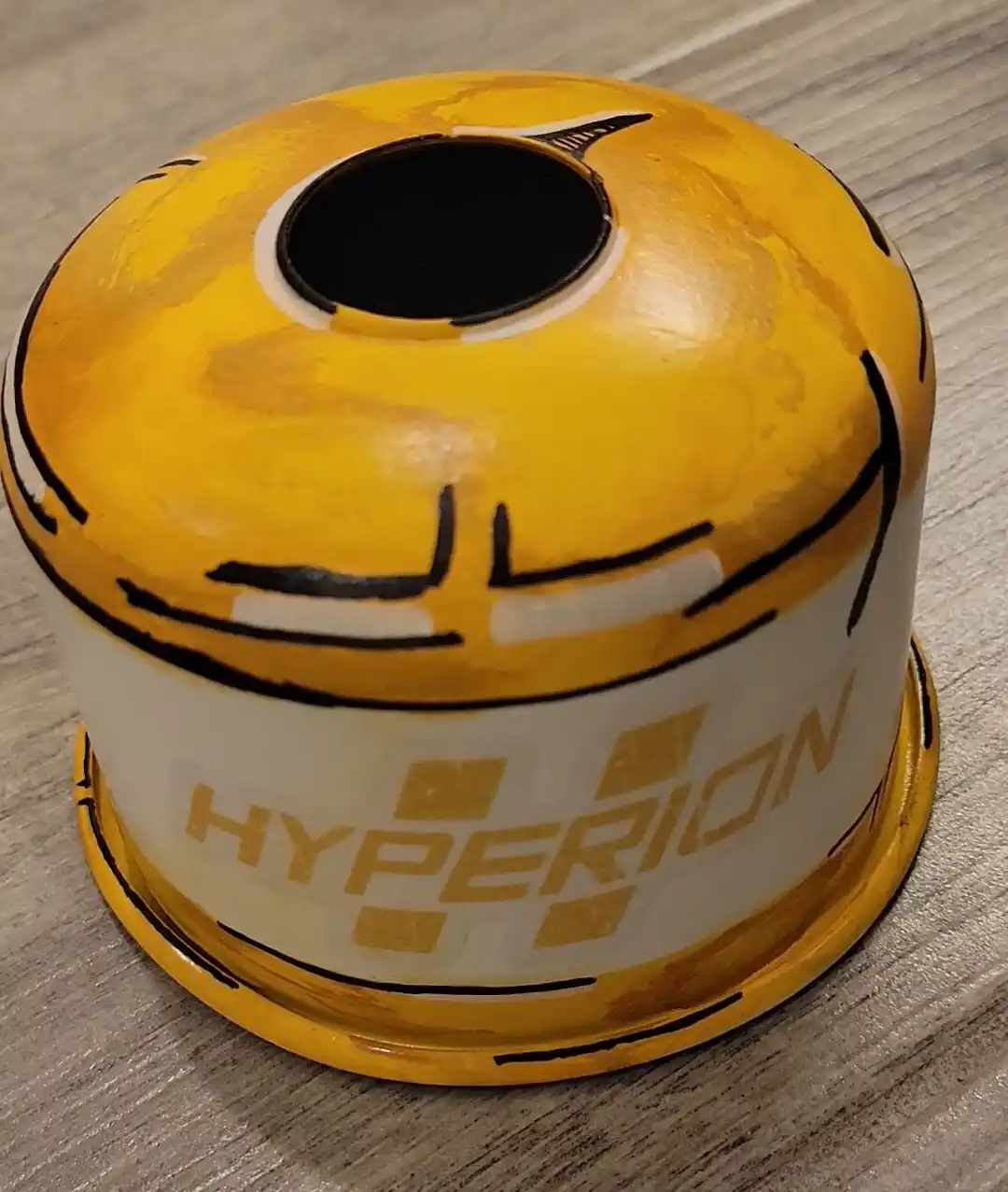 A yellow and white cylindrical object, resembling a gas canister or fuel tank, is painted with crude black lines to look…
