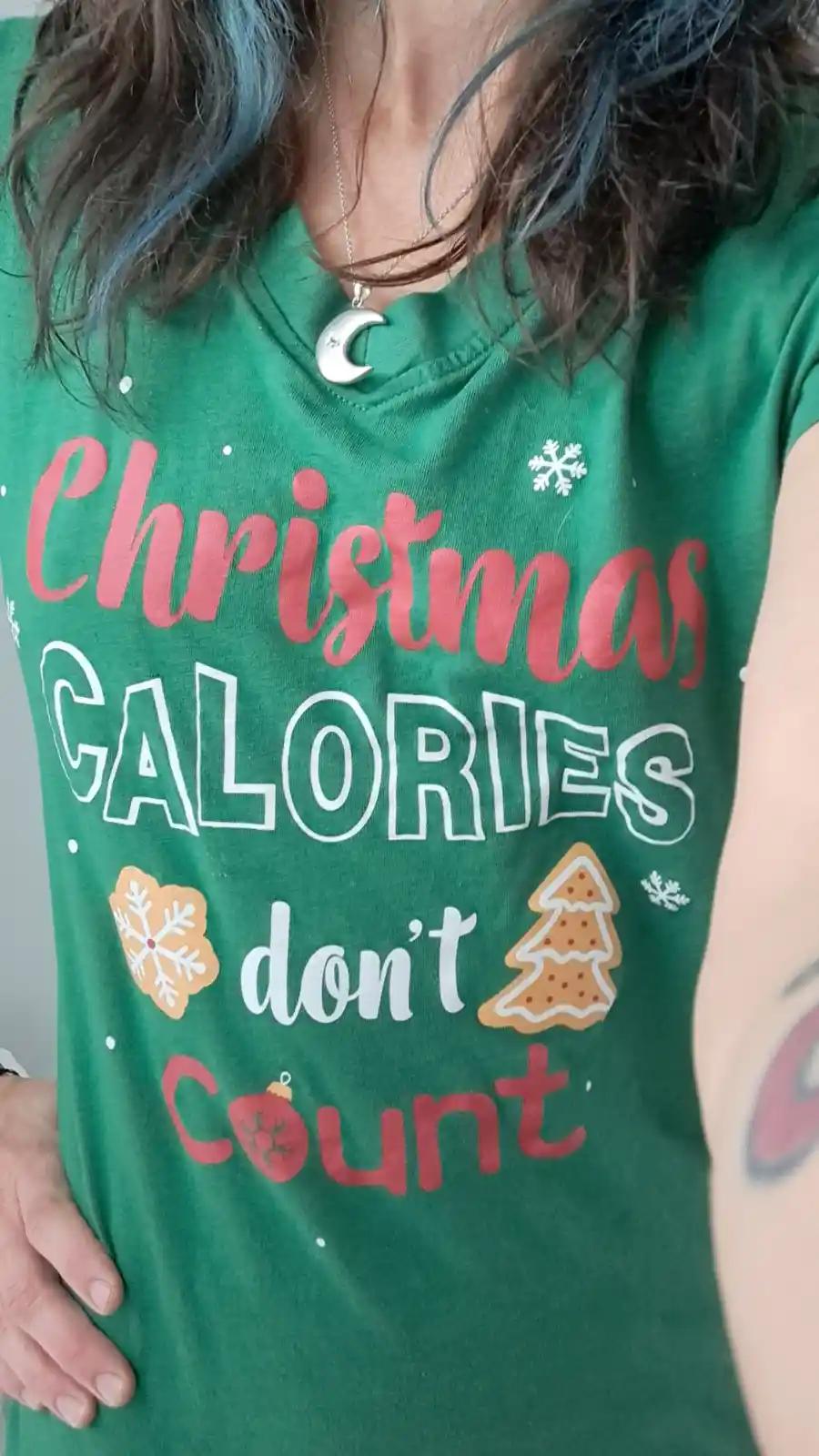 A person wearing a green holiday t-shirt with the text 'Christmas CALORIES don't Count' in red and white lettering…
